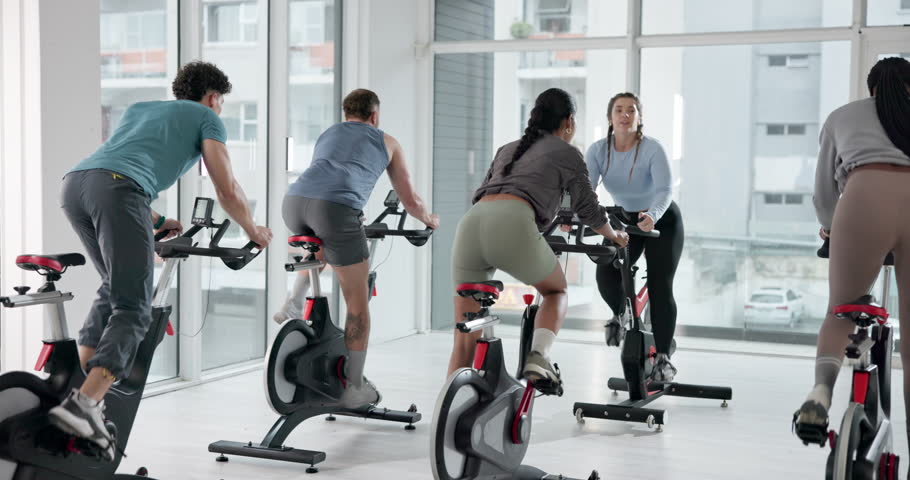 People, coach and fitness with bike at gym for exercise, cardio training and indoor cycling. Smile, group and instructor with bicycle machine, endurance workout and intense performance at spin class