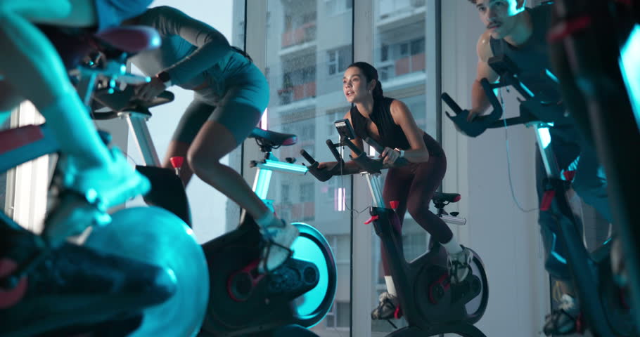 Cycling, spin class and people in gym with lights for cardio workout, exercise and training. Sports, health club and group on bike machine for endurance, core strength and challenge for wellness
