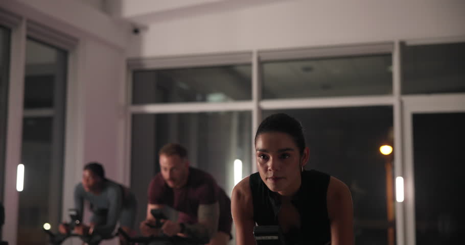 Exercise, group and stationary bike with people in spin class for cardio improvement at night. Cycling, fitness and performance with athletes riding equipment in gym for late evening challenge