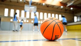 Orange basketball resting on hardwood court with blurred players practicing in background during dynamic training session - Powered by Shutterstock - Get 15% off with code: PIKWIZARD15