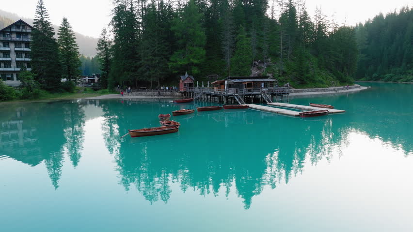 Boats rest on still lake Braies in Dolomites with rugged tree reflections and glowing light across water