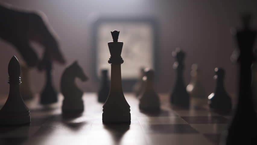 A man moves chess pieces on a chessboard in a dimly lit room