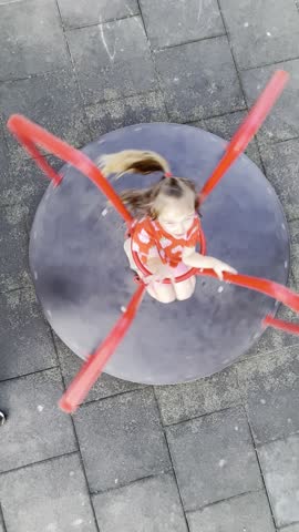 A little girl is riding a children's carousel. The girl is spinning fast on the carousel, having fun and enjoying the process. A child is walking outside on a playground in the fresh air.
