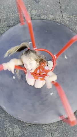 A little girl is riding a children's carousel. The girl is spinning fast on the carousel, having fun and enjoying the process. A child is walking outside on a playground in the fresh air.