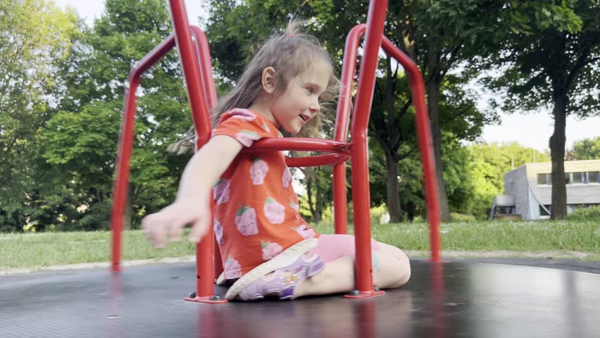 A little girl is riding a children's carousel. The girl is spinning fast on the carousel, having fun and enjoying the process. A child is walking outside on a playground in the fresh air.
