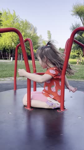 A little girl is riding a children's carousel. The girl is spinning fast on the carousel, having fun and enjoying the process. A child is walking outside on a playground in the fresh air.