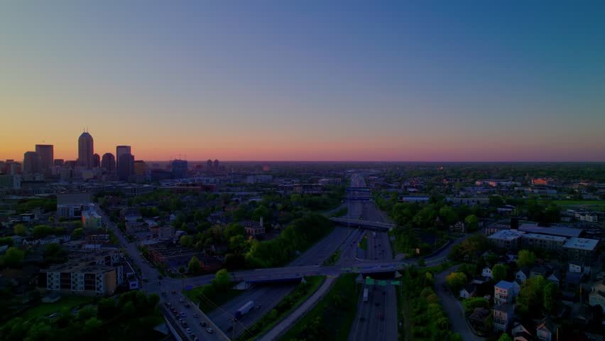 Stunning aerial footage of Indianapolis skyline during sunset, featuring busy highways and urban neighborhoods.