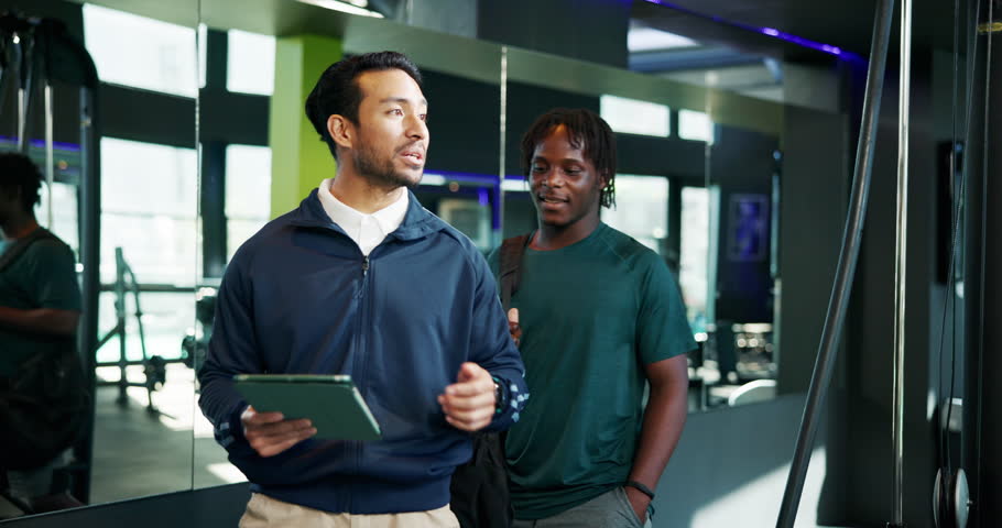 Conversation, man and personal trainer with tablet in club for planning of training program. App, consulting or exercise with client and fitness coach in gym for development of workout schedule