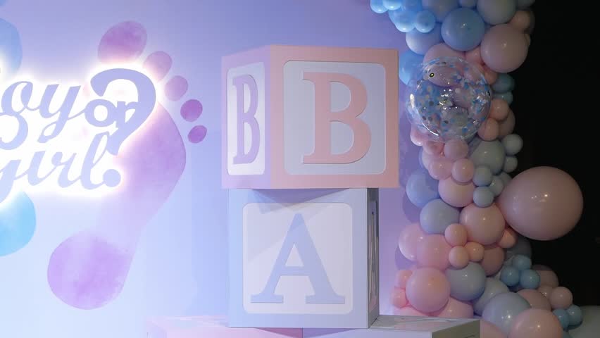 A large beautiful photo zone with pink and blue balloons and the inscription BOY OR GIRL at a gender party. Huge cubes with the inscription BABY. 