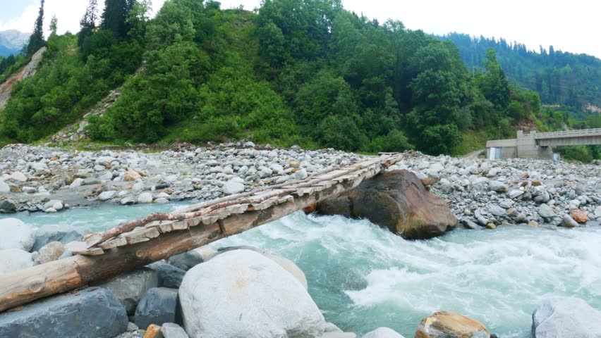4K shot of Beautiful wooden pedestrian bridge over a fast mountain river at Manali, Himachal Pradesh, India. Beas river in Solang Valley during summer season. Nature and travel background.

