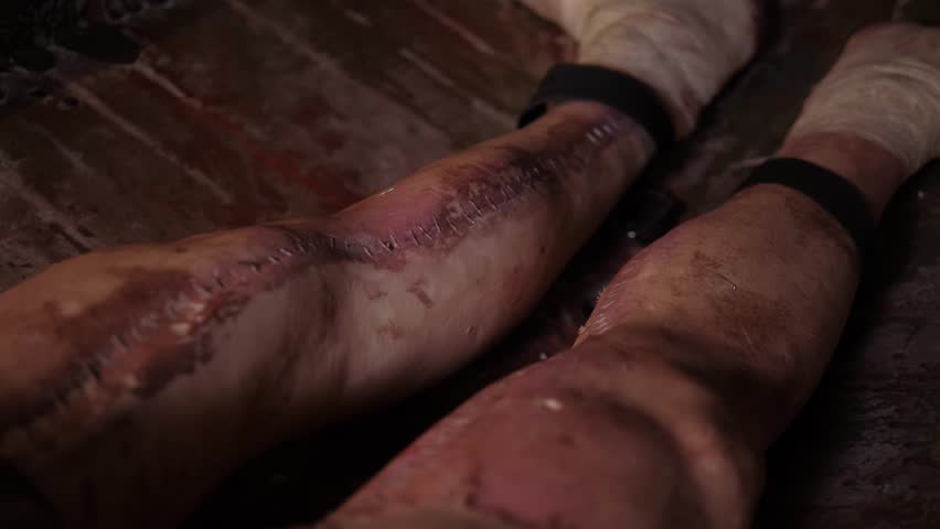 A close-up of creepy bandaged legs with the scars of a plastic mannequin in a panic room or a quest room. A mannequin in the form of a corpse in a creepy room lies on a table with a dirty cloth.