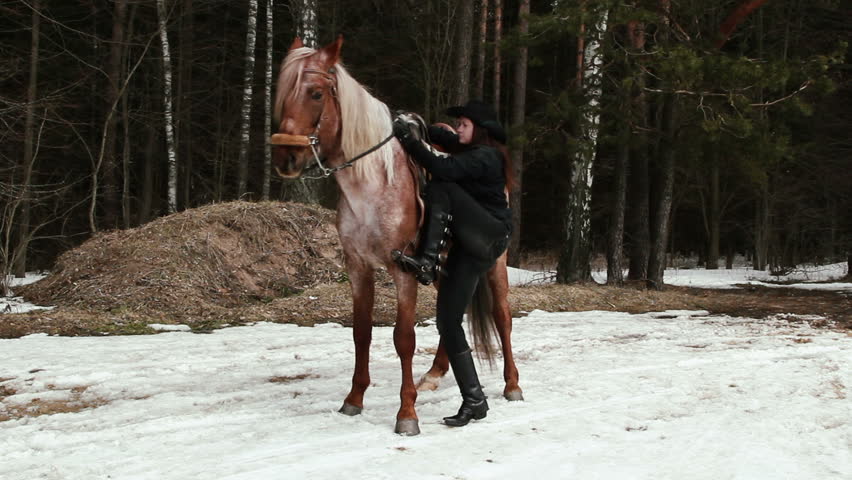 Cowboy woman climbs on a horse in winter