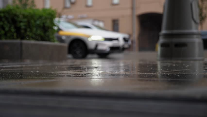 A blurry image of a traffic jam in the city during the rain, raindrops on the sidewalk in the foreground. Taxis and trucks are driving slowly in traffic in the rain.