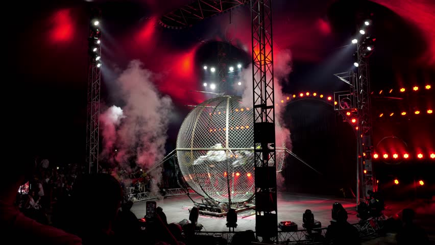 A dangerous stunt show with motorcyclists in a circus. Three stunt actors ride motorcycles in a metal round cage at a circus performance, a dangerous stunt.