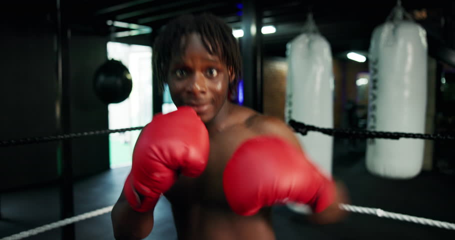 Boxing, gloves and face of black man in gym with fitness, self defense or training for match. POV, knockout and portrait of African boxer with power punching practice for workout in sports center.