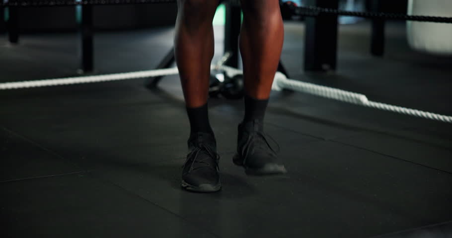 Feet, person and skipping rope at gym for fitness, warm up routine and preparation for boxing match. Legs, boxer and jump with equipment for getting ready, endurance training and workout challenge