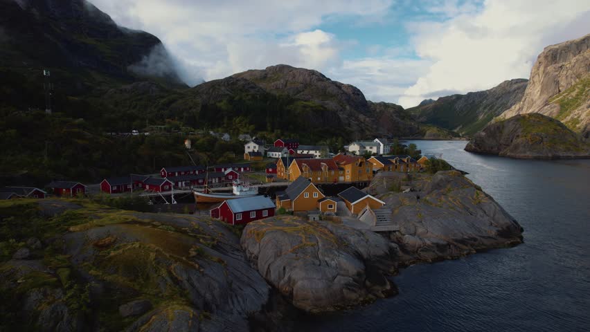 Coastal Norway village with traditional red and yellow cabins, mountains, and clear blue sea. Lofoten