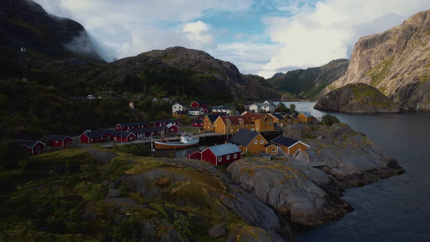 Lofoten village with iconic red and yellow rorbuer cabins and surrounding mountain seascape. Aerial.