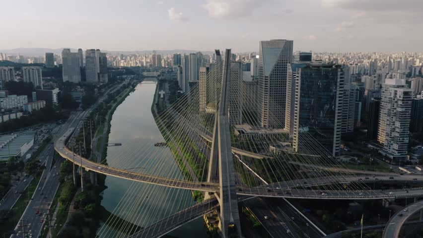 Aerial zoom out revealing the full structure of Octavio Frias de Oliveira Bridge and its surrounding modern skyline in Sao Paulo, Brazil.
