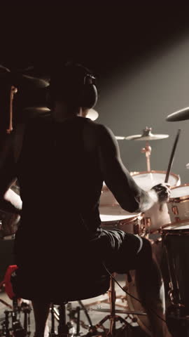 Dark silhouette of musician playing drum set, rehearsal or gig of rock band. Feeling rhythm, energy and power of music, contemporary musical style, vertical video, man with wireless headphones