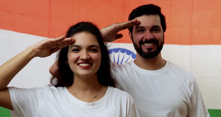 Couple with Indian national flag celebrating with fist and saluting proudly against white background, smiling and confident during Republic Day or Independence Day celebration, looking at camera
