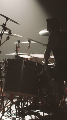 Rehearsal or gig of modern rock band, silhouette of drummer at drum set in darkness, vertical video. Talented musician beating rhythm and expressing emotions, professional drummer striking cymbals