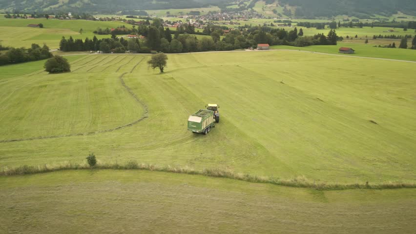 A drone orbits around a tractor turning in a golden Allgäu field during farm work, with no mountains or lakes in view.