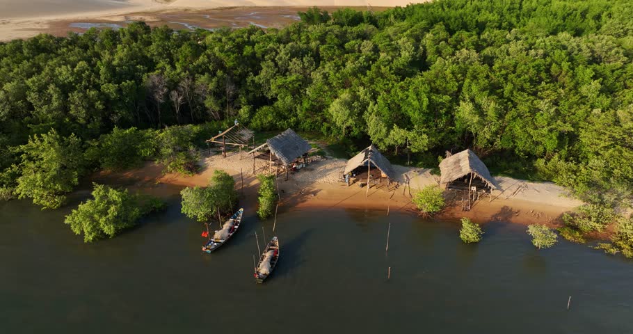 Indigenous people wooden huts near Parnaiba river tributary surrounding mangrove forest, wooden huts for housing near river shore, desert in background, Drone shot