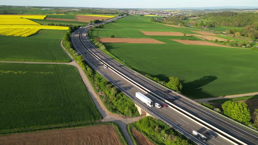 A drone view of Autobahn 5 with traffic surrounded by agriculture fields on a sunny day in Butzbach, Germany