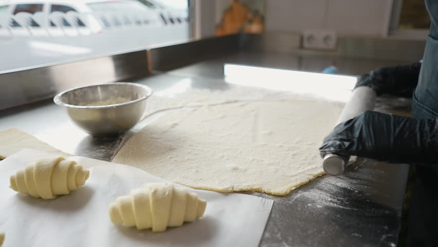 Baker rolls out dough for croissants on floured table
