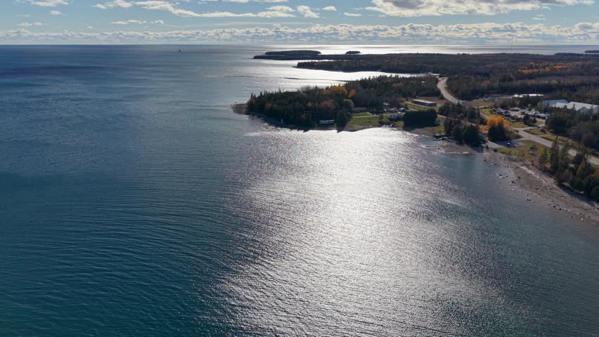 Aerial view of sun reflecting on Lake Huron with forested shoreline and clouds over the Upper Peninsula of Michigan
