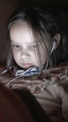 A young child intently using a device with headphones in a dim environment, showcasing modern tech engagement.