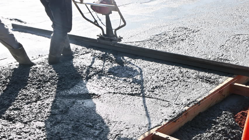 Workers are using concrete leveling tool to smooth out freshly poured cement at construction site.