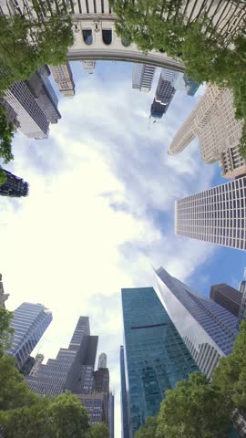 Fisheye lens view looking straight up at towering Manhattan skyscrapers, framed by leafy trees. A dynamic and immersive shot capturing the vertical scale and energy of New York City architecture. 1467