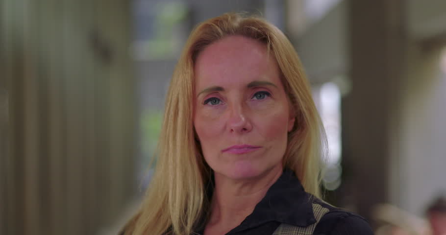 Businesswoman with serious facial expression looking directly at camera in modern office hallway