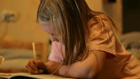 Young Caucasian girl is write in textbook with the pen sitting at a table at home filmed in closeup. Female child is doing homework being concentrated and serious. School tasks and studying concept - Powered by Shutterstock - Get 15% off with code: PIKWIZARD15
