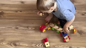 Toddler playing alone with a colorful wooden train on a wooden floor. Educational and imaginative play at home. Focus on hands and toy movement. Calm and cozy atmosphere - Powered by Shutterstock - Get 15% off with code: PIKWIZARD15