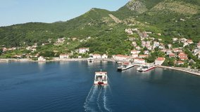 Aerial view of a passenger ferry sailing in the Bay of Kotor against the backdrop of a picturesque mountain coastline and a seaside town on a sunny day - Powered by Shutterstock - Get 15% off with code: PIKWIZARD15