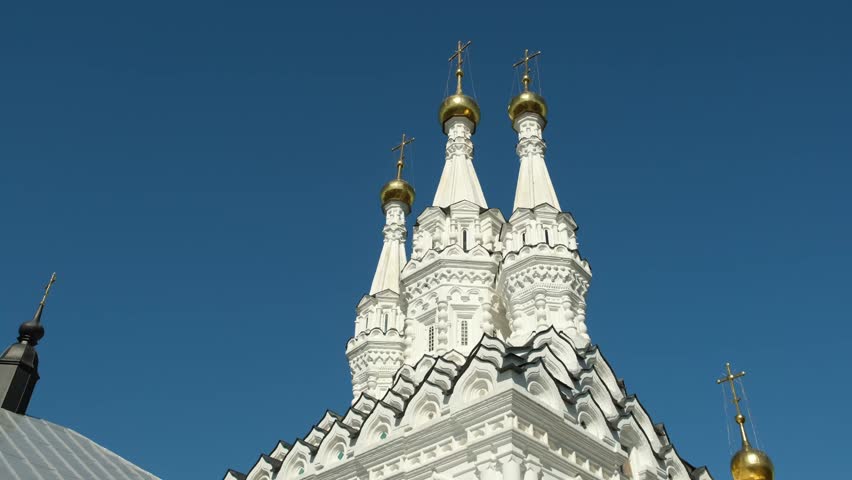 The video highlights intricate details of a striking church featuring three towering spires adorned with golden domes under a bright blue sky, showcasing beautiful architecture.