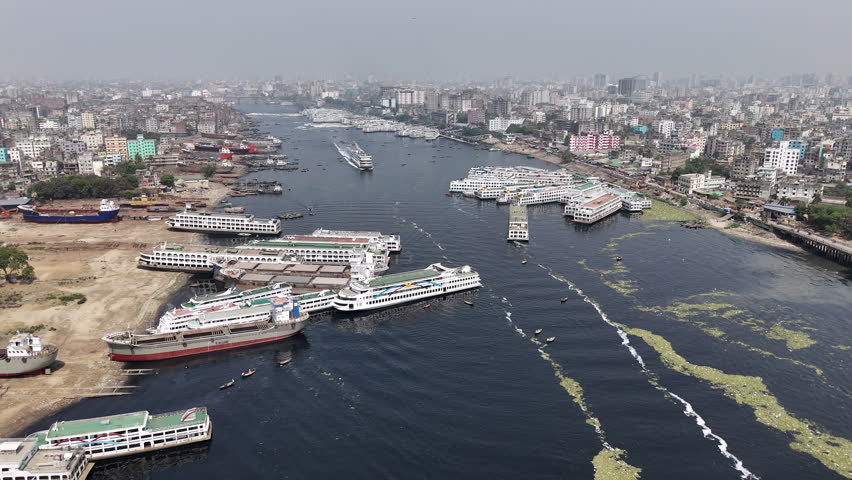 Cinematic descending aerial shot of the polluted waters and ferries parked along the shore in the Buriganga river in Dhaka, Bangladesh