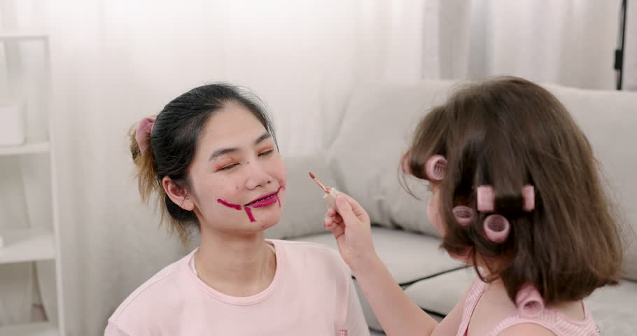 Asian girl using cosmetic sponge to pat blush on single mother face during warm family activity at home highlighting close emotional connection between daughter and adult parent