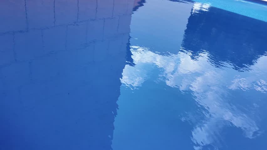 A pool with a blue surface and a reflection of a building in the water. Scene is calm and serene, as the water appears still and peaceful