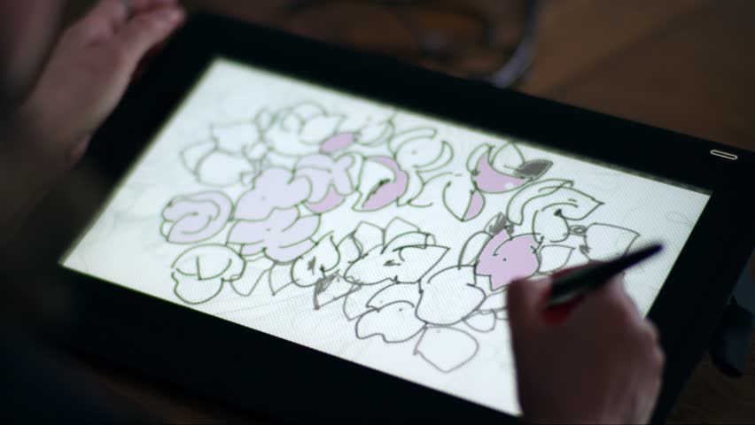 Digital floral sketching on graphic tablet. A hand drawing stylised flowers with pink accents on a digital tablet using a pen. Close-up view of the creative process.