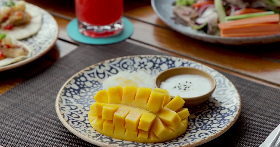 Tropical dessert Thailand with sliced mango, sticky rice, coconut sauce on decorative plate. Asian cuisine, vibrant colors, culinary delight. Mango sticky rice.
