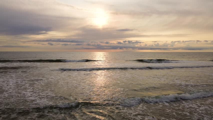 Waves roll onto the scenic Danish west coast, where sandy beaches meet the vast horizon under a soft sunset.