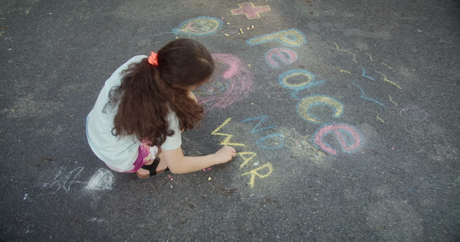 Little girl writing peace with chalk. Cute little girl drawing peace on the pavement with chalk. Protest against war, Russia's invasion of Ukraine.