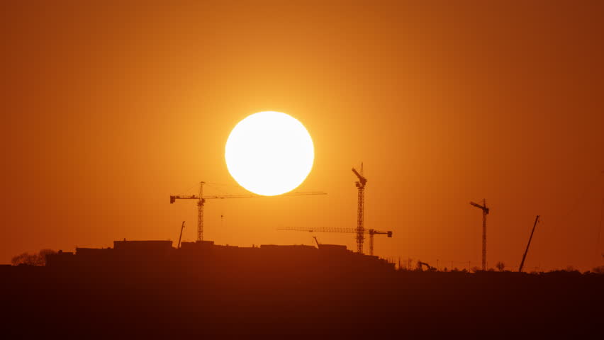 Sunset silhouette time lapse of construction site with cranes. Building and industry scene capture on telephoto lens.