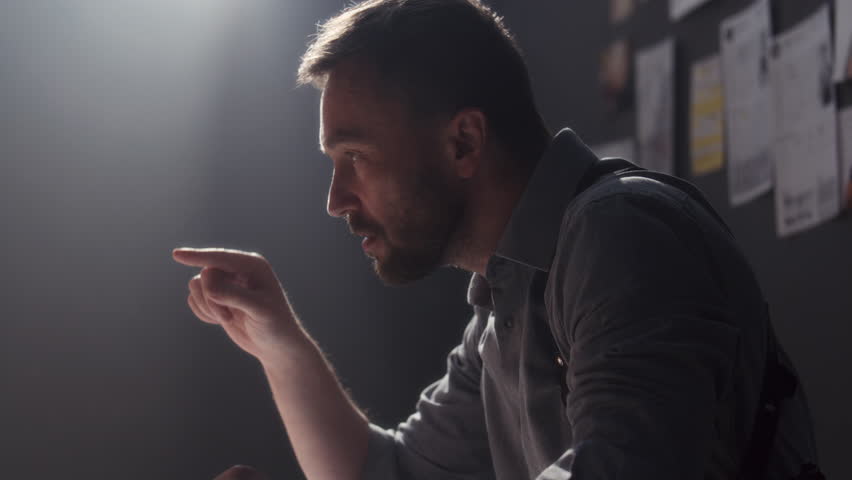 Assertive investigator pointing finger, showing mugshot photo and talking to suspect during intense interrogation in police interview room