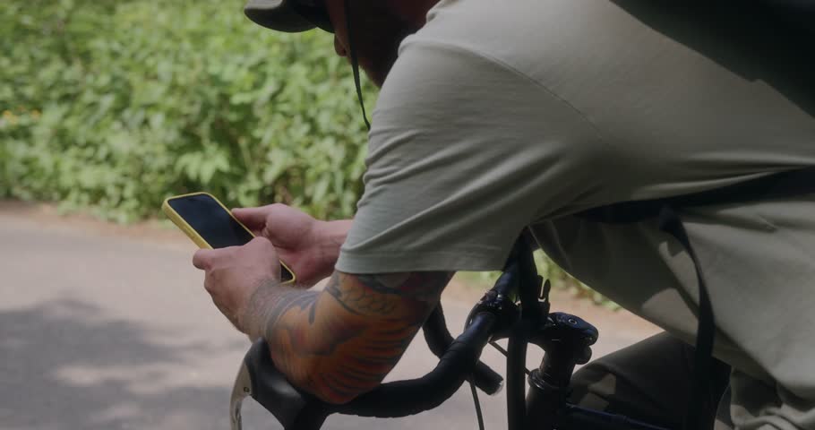 A detailed over-the-shoulder shot shows a man checking his phone while glancing down a quiet forest road. A crossroads between two worlds - digital and natural. High quality 4k footage