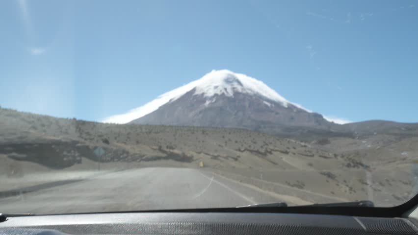 Navigating serpentine mountain highway, vehicle traversing scenic route near iconic Chimborazo volcano, revealing breathtaking Ecuadorian landscape under bright summer sky